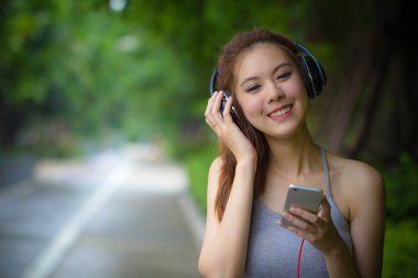 Rahatlatıcı ve kulaklık ile müzik dinleme sırasında şarkı smartphone kullanan mutlu genç kadın. Asyalı kız heppiness kavramı duygu kulaklık kullanarak. Güzel moda kadın model müzik keyfi.