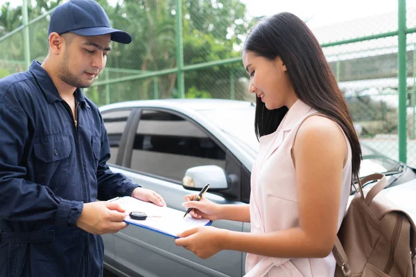 Technician repairman giving car key to woman in workshop. mechanic repair client car in auto service shop. female customer sign paper insurance bill contact in garage. Fixing car concept.
