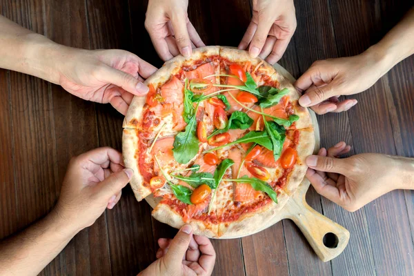 İnsanlar ellerini alarak dilimleri, somon Pizza roka ve domates ile