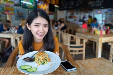 El kızarmış holding arka plan kalabalık kişi ile restoranda masa plaka mealon pirinç. Genç Asyalı kadın Tay yemek yeme. Mutlu kız pilav ve sebze soslu domuz eti yiyor.