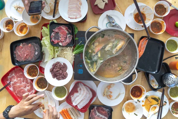 As pessoas gostam de comer Shabu Sukiyaki, comida japonesa juntos vista superior. Sukiyaki Shabu Hot Pot refeição com a família. grupo de amigos tomando café da manhã na mesa, Homem segurando smartphone tirando foto . — Fotografia de Stock