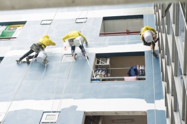 Ruloüzerinde asılı ressamlar, duvara renk boyama. Silindir fırça ile Cephe oluşturucu, yüksek bina inşaat üzerinde çalışıyor.