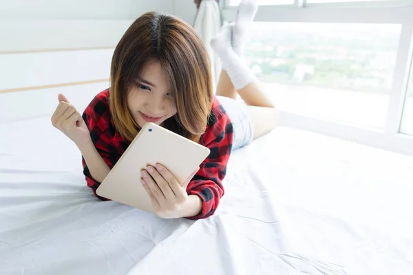 Lycklig ung kvinna som ligger på sängen med Tablet PC. — Stockfoto
