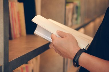 Kütüphanede kitap okuyan genç adam, kapat. Üniversite öğrencisiyim. Kitap okuyorum. Üniversite konsepti hakkında bilgi sahibiyim. Sınav için sıkı çalış.