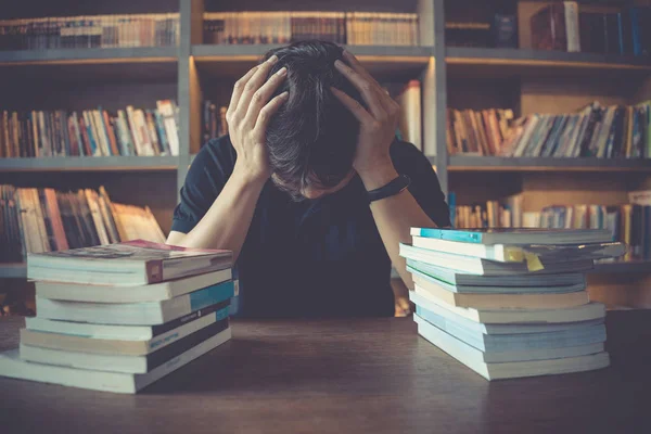 Stres ve yorgun adam zihinsel baskı altında kitap okurken kütüphanede sınav hazırlanıyor. İşadamı, halk kütüphanesinde masa başında kitap yığınları üzerinde çok çalıştıklarını vurguladı.