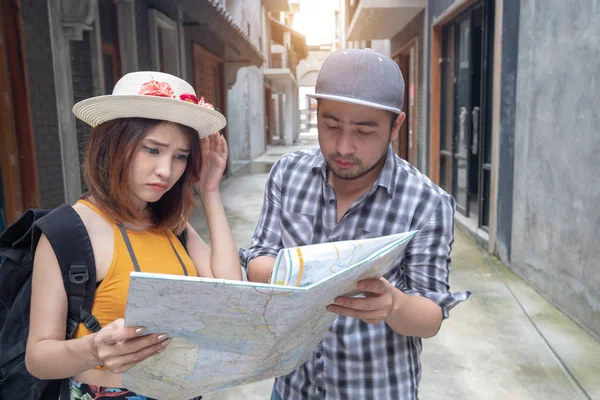 Jovem casal asiático segurando mapa olhando direção em férias de lua de mel. As pessoas turísticas no verão perderam em conjunto na viagem de férias. Amante namoro encontrar local de destino no mapa se sentindo perdido . — Fotografia de Stock