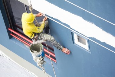 rulo asılı ressamlar, bina duvarında renk boyama. silindir fırça ile cephe oluşturucu işçi, yüksek bina üzerinde çalışıyor. şehirde asansör halat kemeri ile güvenlik inşaatı. 