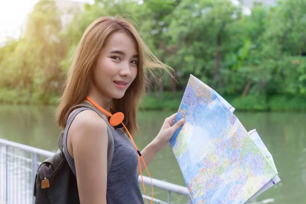 Mulher viajante jovem olhando para o mapa na natureza ao ar livre estação verde. Menina asiática feliz segurando mapa plano para viagem sorrindo para a câmera. Conceito de férias de viagem turística . — Fotografia de Stock