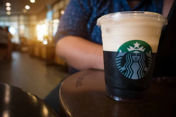 Chiangmai, thailand-juli 22, 2019: prickelnder Nitro-Kaltgebrühkaffee in Plastik-Take-away-Tasse fertig zum Trinken im Starbucks Store Café. Starbucks Kaffee Markenlogo auf Nitro American Kaffee kaltes Gebräu Getränk auf dem Tisch mit Mann sitzt im Hintergrund — Stockfoto