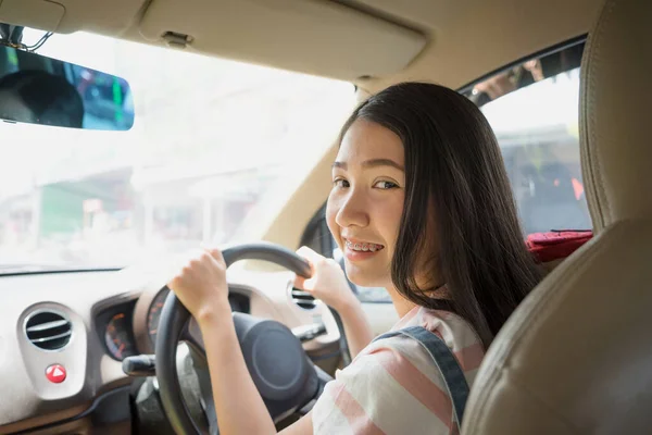 Giovane donna asiatica guida auto mantiene ruota girando sorridente guardando i passeggeri sul sedile posteriore godere di servizio . — Foto Stock