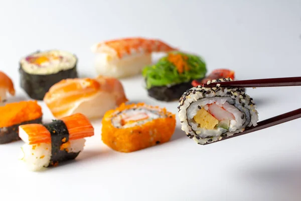 Eating fresh Sushi Maki and Niguiri roll menu with chopsticks. Sushi roll japanese food in restaurant. California Sushi roll set with vegetables and caviar closeup on white background. — ストック写真