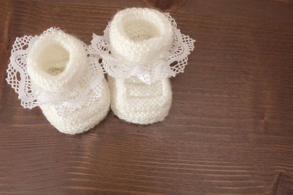 Knitted baby slippers are white with a lace on a wooden table