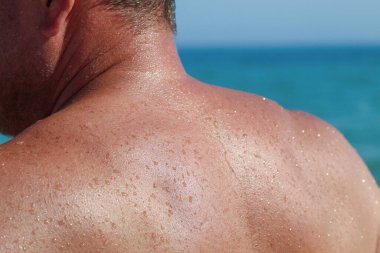 Denizde yüzdükten sonra su damlacıkları olan bir erkek omzunun yakın çekimi, yazı, tatili, güneşi, tazeliği ve rahatlamayı simgeliyor..