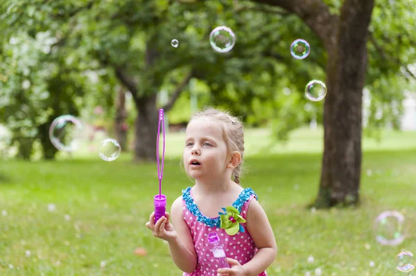 夏の公園でシャボン玉を吹いているカラフルなドレスの少女 — ストック写真