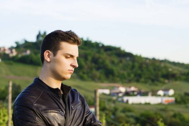 Güzel bir genç adam bir deri ceketli ikindilerde tepelerin arka planda duruyor