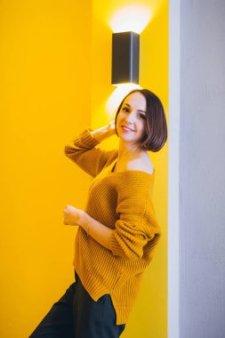 Genç güzel kadın sarı duvara poz. Tonlama.