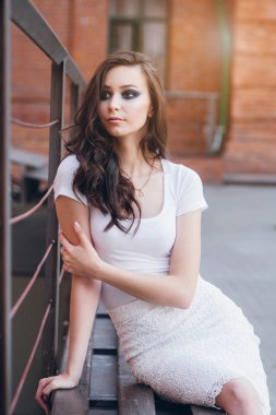 Zarif beyaz elbiseli uzun saçlı Genç güzel esmer kız. Gün batımında akşamları şehrin sokaklarında yürüyen kadın.