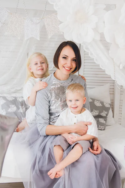 Mutlu anne, kızı ve oğlu yatakta kıyafetler içinde oturuyor. Balonlar ile tatil. Tonlama.