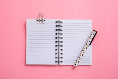 Not defteri ve kalem pembe bir arka plan üzerinde. Düz yatıyordu kompozisyon. Masanın üzerinde ofis, banka donatımı.