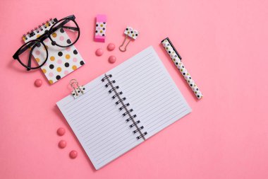 Not defteri, kalem ve pembe bir arka plan üzerinde gözlük. Düz ley kompozisyon. Masanın üzerinde ofis, banka donatımı.