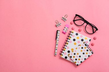 Not defteri, kalem ve pembe bir arka plan üzerinde gözlük. Düz ley kompozisyon. Masanın üzerinde ofis, banka donatımı.
