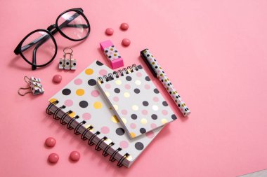 Not defteri, kalem ve pembe bir arka plan üzerinde gözlük. Düz ley kompozisyon. Masanın üzerinde ofis, banka donatımı.