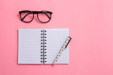 Not defteri, kalem ve pembe bir arka plan üzerinde gözlük. Düz ley kompozisyon. Masanın üzerinde ofis, banka donatımı.