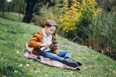 Sevimli çocuk yürür ve renkli bir sonbahar Park teşkil etmektedir. Çocuk çimenlerin üzerine oturmuş bir termos sıcak çay dökülen. Tonlama.