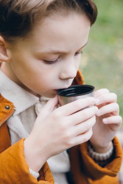Sevimli çocuk yürür ve renkli bir sonbahar Park teşkil etmektedir. Çocuk üzerinden çimenlerin üzerine oturmuş bir termos sıcak çay içer. Tonlama.