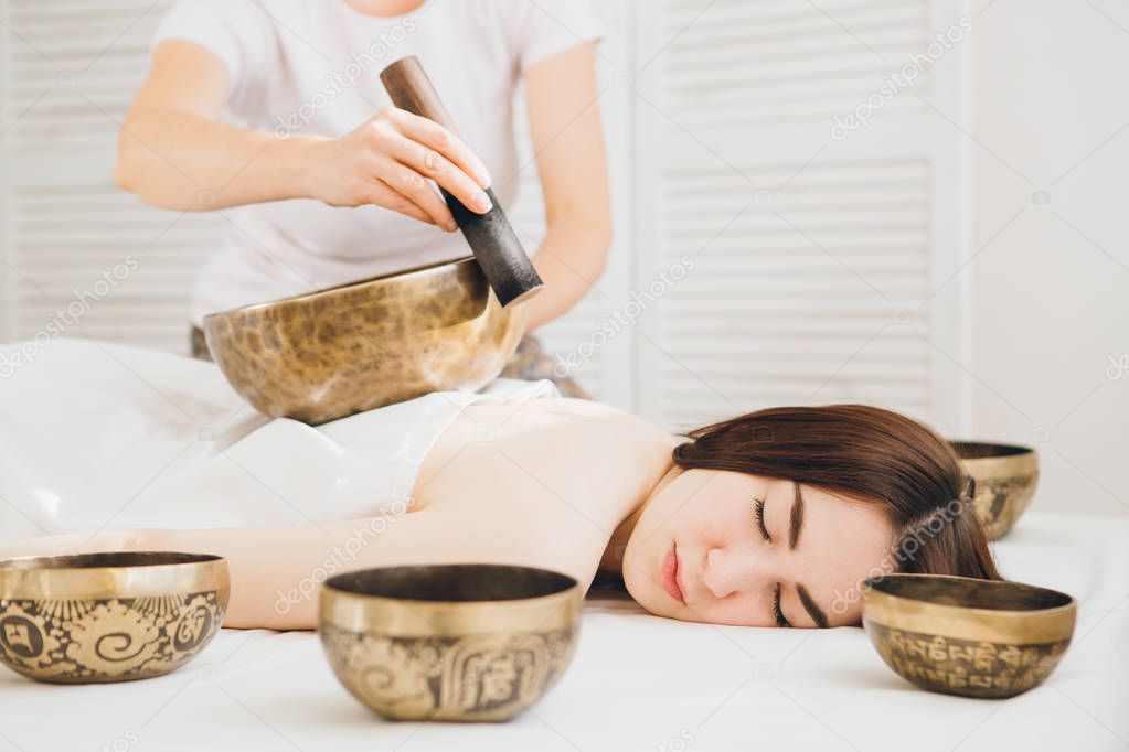 Young beautiful girl doing massage therapy singing bowls in the Spa. The concept of relaxation and alternative medicine. Toning.
