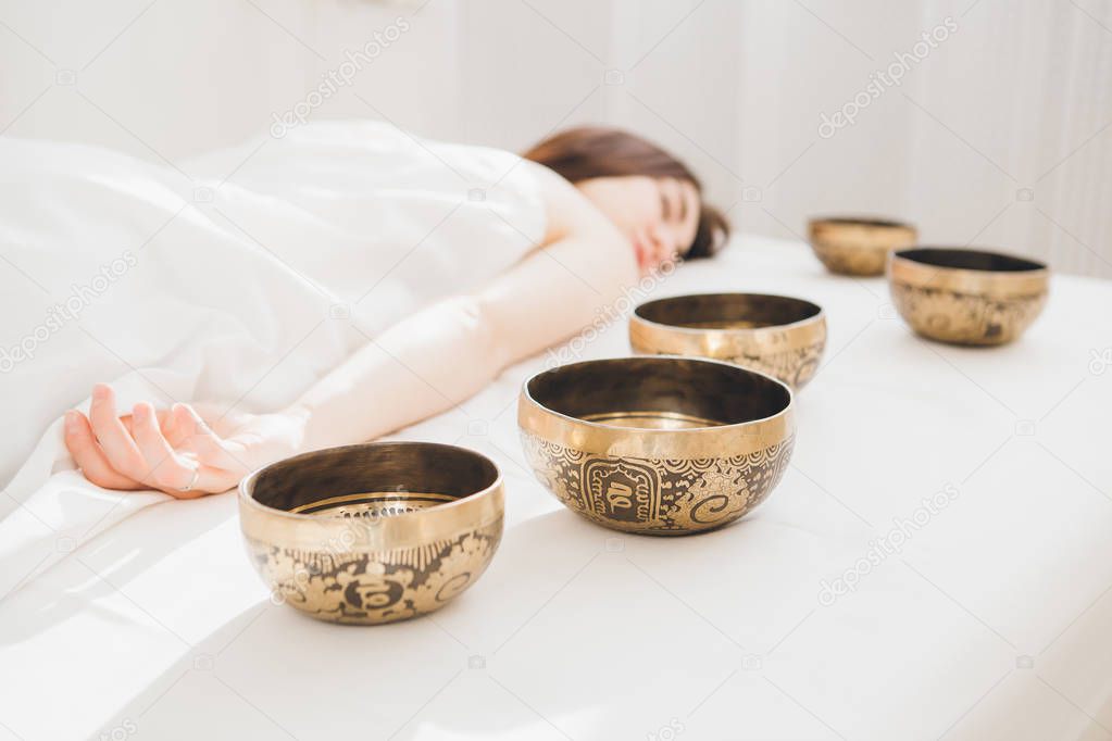 Young beautiful girl doing massage therapy singing bowls in the Spa. The concept of relaxation and alternative medicine. Toning.