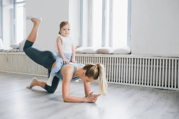 Genç sportif anne ve bebek kız egzersizleri birlikte spor yapın. Üst ve alt sağlıklı geliştirme, fitness ve dinlenme. Sağlıklı yaşam konsepti fotoğraf. Tonlama.