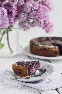 Homemade blueberry pie on a white wooden table next to a vase of lilacs. Gentle toning. Selective focus.