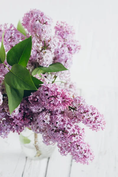 Bouquet of lush lilac in a vase on a white wooden table. Gentle toning. Selective focus.