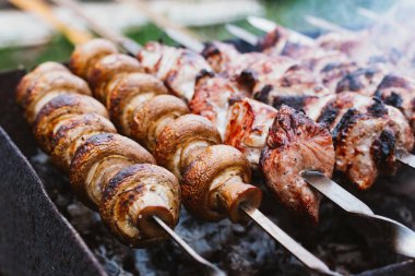Marinated pieces of meat and mushrooms are grilled on charcoal skewers. Shashlik or kebab. The concept of the barbecue. Selective focus.