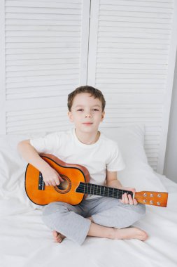 Çocuk yatağa oturan küçük bir gitar çalmak 