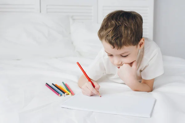 Chlapec se kreslí s barevné tužky, sedí na posteli — Stock fotografie