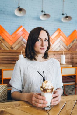 Kadın, krema ve kurabiyelerle süslenmiş güzel bir milkshake içer. 