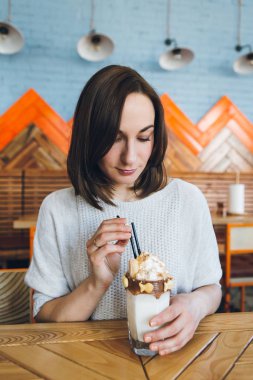 Kadın, krema ve kurabiyelerle süslenmiş güzel bir milkshake içer. 