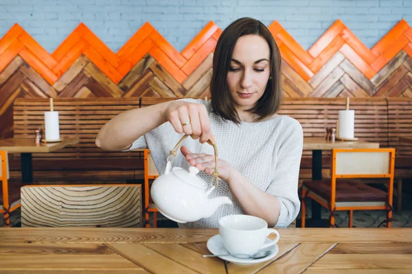 Kvinna häller grönt te från en tekanna i en kopp i ett café — Stockfoto