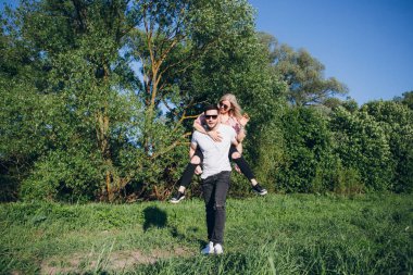 Yaz aylarında doğada sarılan ve gülümseyen bir adamın sırtında oturan kız