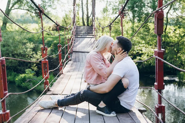 Jovem casal cara e menina na ponte sobre o rio e beijo — Fotografia de Stock