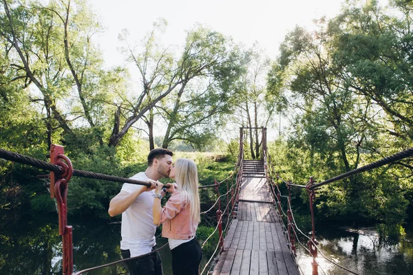 Jovem casal cara e menina na ponte sobre o rio e beijo — Fotografia de Stock
