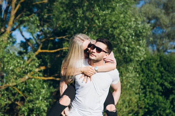 Menina sentada nas costas de um homem abraçando e sorrindo na natureza no verão — Fotografia de Stock