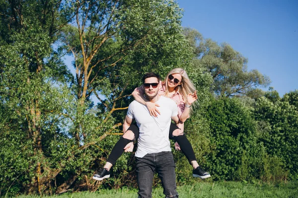 Mädchen sitzt auf dem Rücken eines Mannes, der sich im Sommer in der Natur umarmt und lächelt — Stockfoto