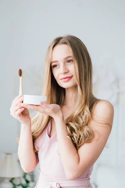 Chica sosteniendo un cepillo de dientes de bambú útil y un frasco de polvo dental — Foto de Stock