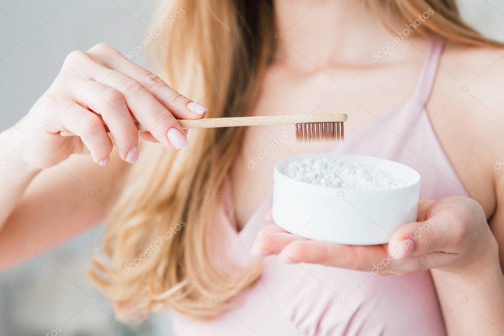 Girl holding a useful bamboo toothbrush and a jar of tooth powder