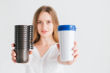 Karşılaştırma için yararlı bir yeniden kullanılabilir cam ve tek kullanımlık plastik bardak tutan Kız