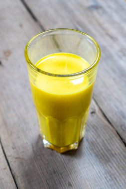 Tahta bir arka planda, cam bir fincandaki altın süt.