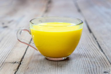 Tahta bir arka planda, cam bir fincandaki altın süt.